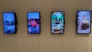 Four digital screens mounted on a wall displaying abstract and scenic images.